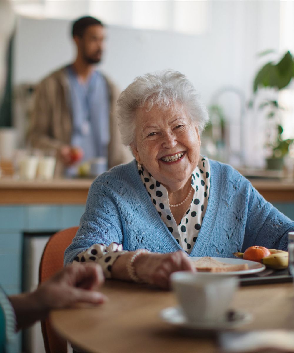 A resident smiling over coffee at the dining table